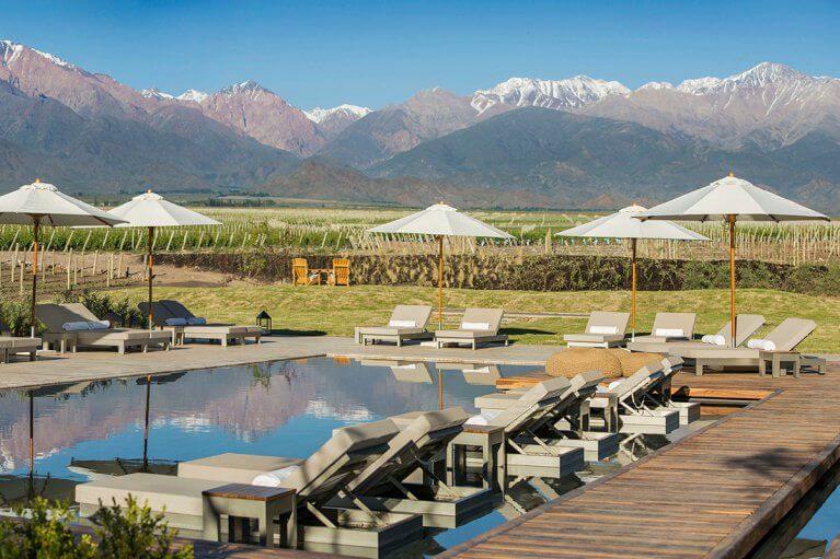 Pool surrounded by lounge chairs, and umbrellas in a vineyard with a stunning view of the Andes Mountains at the Vines Resort