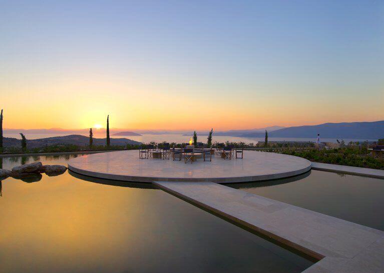 Outdoor pool with seating area in middle and view of sea at Amanzoe luxury resort on Peloponnese peninsula